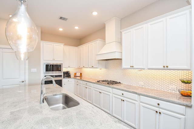 13910 Paseo De La Paz Pl, Cypress, TX 77433 - kitchen featuring appliances with stainless steel finishes, custom range hood, white cabinetry, backsplash, and light stone countertops
