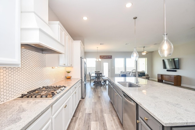 13910 Paseo De La Paz Pl, Cypress, TX 77433 - kitchen with custom range hood, stainless steel appliances, white cabinetry, a large island with sink, and light wood-style floors