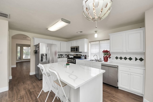 3622 Stratford Town Ln, Sugar Land, TX 77498 - kitchen with stainless steel appliances, arched walkways, white cabinetry, a center island, and dark wood-style flooring