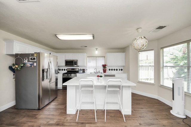3622 Stratford Town Ln, Sugar Land, TX 77498 - kitchen with appliances with stainless steel finishes, white cabinetry, a kitchen island, dark wood-style flooring, and a kitchen bar