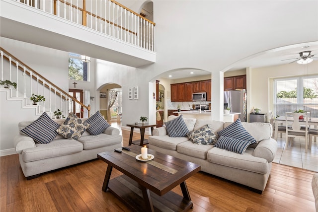 23602 Hawkins Creek Ct, Katy, TX 77494 - living room with arched walkways, a high ceiling, a ceiling fan, light wood-style floors, and stairs
