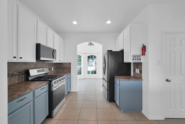 19210 Kent Park Dr, Tomball, TX 77375 - kitchen featuring stainless steel appliances, arched walkways, dark countertops, white cabinetry, and backsplash