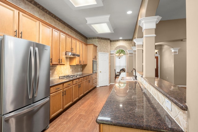 31406 Spica St, Tomball, TX 77375 - kitchen featuring appliances with stainless steel finishes, light wood-type flooring, under cabinet range hood, backsplash, and dark stone counters