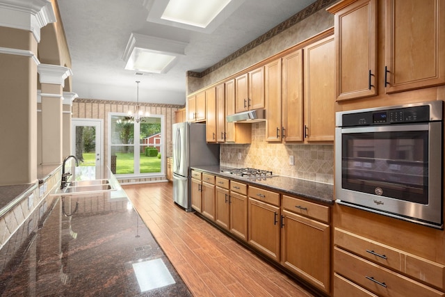 31406 Spica St, Tomball, TX 77375 - kitchen featuring stainless steel appliances, wallpapered walls, light wood-style floors, decorative light fixtures, and decorative backsplash