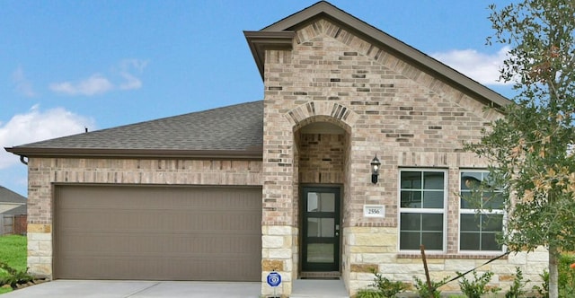 2556 Newport Breeze Dr, Katy, TX 77493 - french country style house featuring driveway, an attached garage, stone siding, a shingled roof, and brick siding