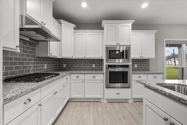 5000 Boreas Dr, Alvin, TX 77511 - kitchen featuring stainless steel appliances, white cabinets, under cabinet range hood, backsplash, and light wood-style floors