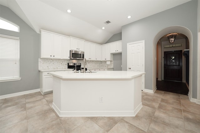 10166 Hidden Creek Falls Ln, Brookshire, TX 77423 - kitchen featuring stainless steel microwave, vaulted ceiling, decorative backsplash, arched walkways, and a kitchen island with sink