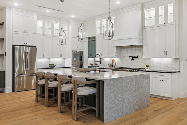 431 W 30th St, Houston, TX 77018 - kitchen with stainless steel appliances, an island with sink, white cabinets, light wood-type flooring, and backsplash