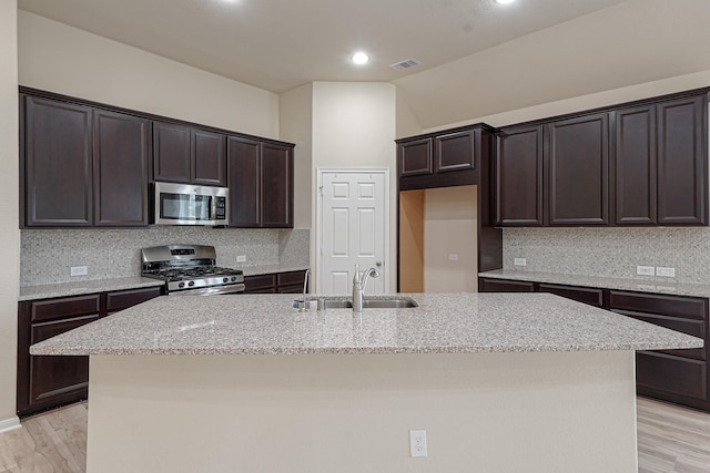 19022 Summer Farm Trl, Richmond, TX 77407 - kitchen with stainless steel appliances, a center island with sink, dark brown cabinetry, light stone countertops, and decorative backsplash
