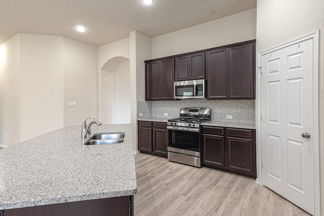 19022 Summer Farm Trl, Richmond, TX 77407 - kitchen with appliances with stainless steel finishes, arched walkways, dark brown cabinets, light wood-type flooring, and backsplash