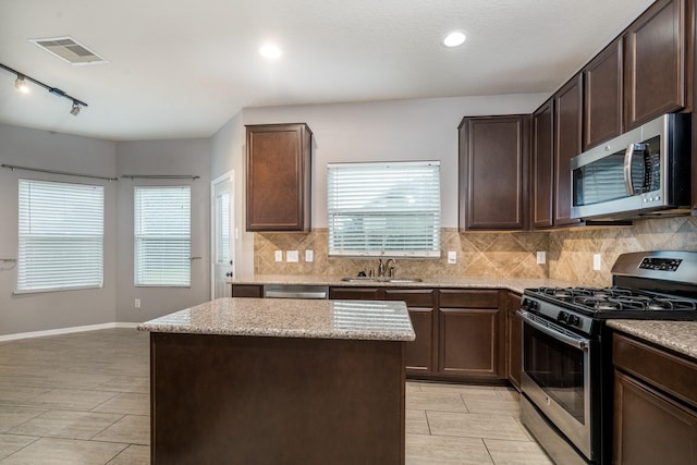 20027 Bayliss Manor Ln, Cypress, TX 77433 - kitchen with appliances with stainless steel finishes, tasteful backsplash, dark brown cabinets, a center island, and light stone countertops