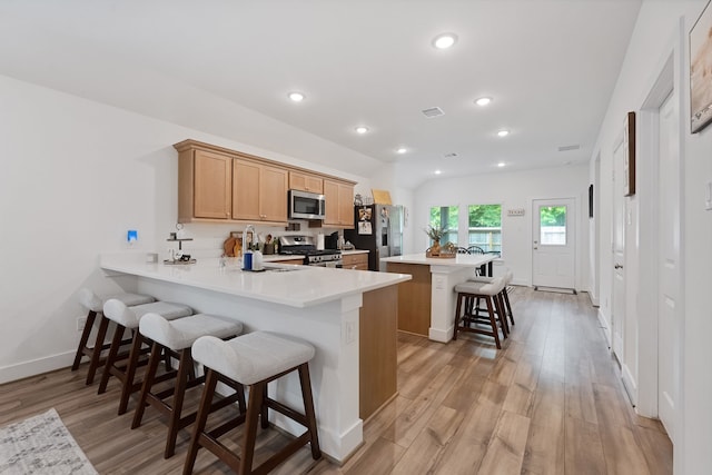 21635 Alberta Forest Cir, Magnolia, TX 77355 - kitchen with stainless steel appliances, a kitchen bar, light wood-style floors, light countertops, and a center island