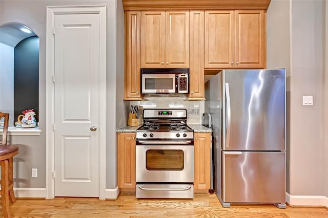 109 Dennis St, Houston, TX 77006 - kitchen with stainless steel appliances, light wood-style floors, light stone countertops, arched walkways, and tasteful backsplash