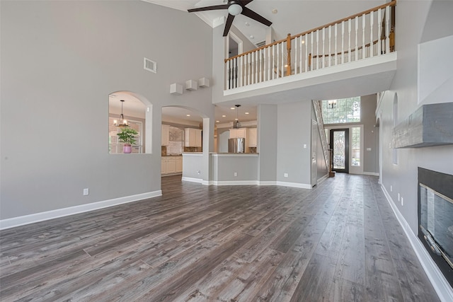 9526 Fern Wood Frst, Houston, TX 77040 - unfurnished living room with a towering ceiling, ceiling fan, dark wood-style flooring, a chandelier, and a glass covered fireplace