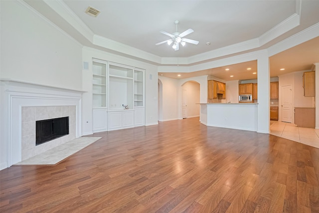 7927 Chateau Point Ln, Houston, TX 77041 - unfurnished living room featuring ceiling fan, crown molding, arched walkways, light wood finished floors, and a tile fireplace