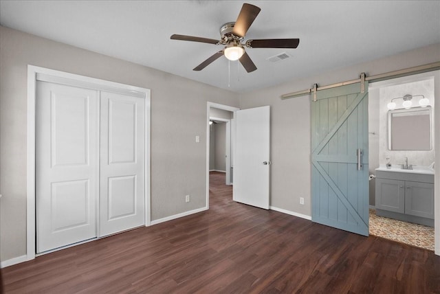 2909 15th Ave N, Texas City, TX 77590 - unfurnished bedroom featuring a barn door, dark wood finished floors, a closet, connected bathroom, and ceiling fan