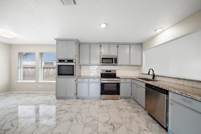 16111 Fan Tail Dr, Crosby, TX 77532 - kitchen with appliances with stainless steel finishes, gray cabinetry, light marble finish flooring, backsplash, and recessed lighting