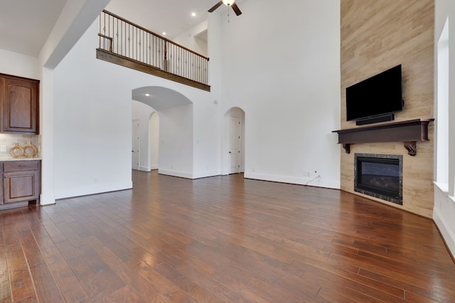 24918 Granite Bluff Ln, Katy, TX 77494 - unfurnished living room featuring a ceiling fan, a fireplace, dark wood-style flooring, a towering ceiling, and arched walkways