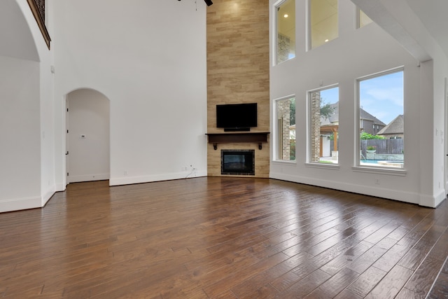 24918 Granite Bluff Ln, Katy, TX 77494 - unfurnished living room featuring a high ceiling, a fireplace, dark wood-type flooring, arched walkways, and a ceiling fan