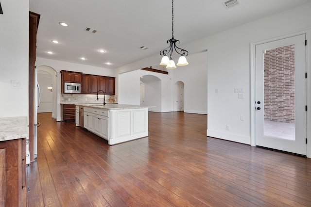 24918 Granite Bluff Ln, Katy, TX 77494 - kitchen with arched walkways, stainless steel microwave, dark wood-style floors, pendant lighting, and a kitchen island with sink