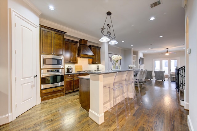 5531 Pine St Unit H, Houston, TX 77081 - kitchen with appliances with stainless steel finishes, custom range hood, wood finished floors, decorative backsplash, and ornamental molding