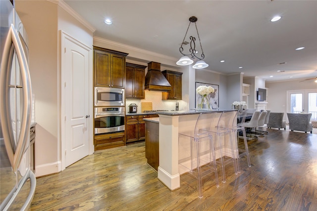 5531 Pine St Unit H, Houston, TX 77081 - kitchen with stainless steel appliances, custom range hood, wood finished floors, backsplash, and a breakfast bar area