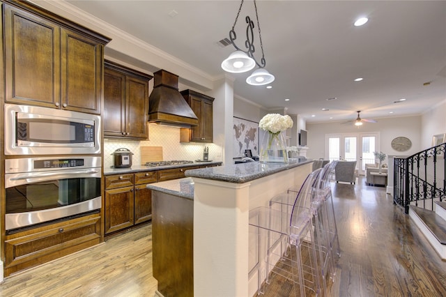 5531 Pine St Unit H, Houston, TX 77081 - kitchen with appliances with stainless steel finishes, custom exhaust hood, light wood-type flooring, dark stone countertops, and an island with sink