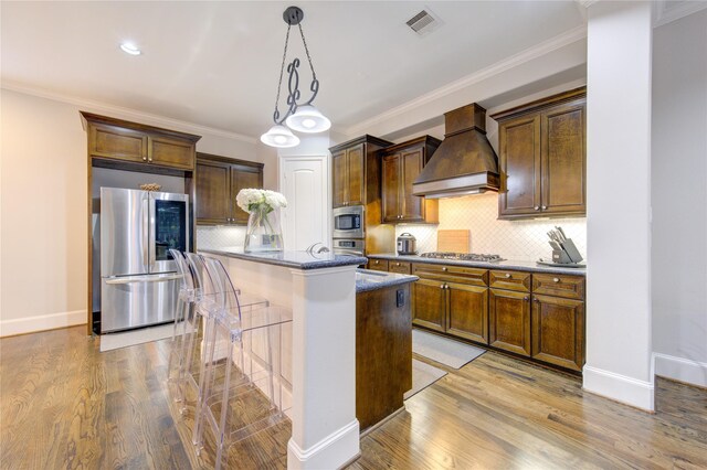 5531 Pine St Unit H, Houston, TX 77081 - kitchen with stainless steel appliances, custom exhaust hood, an island with sink, light wood-type flooring, and a kitchen bar