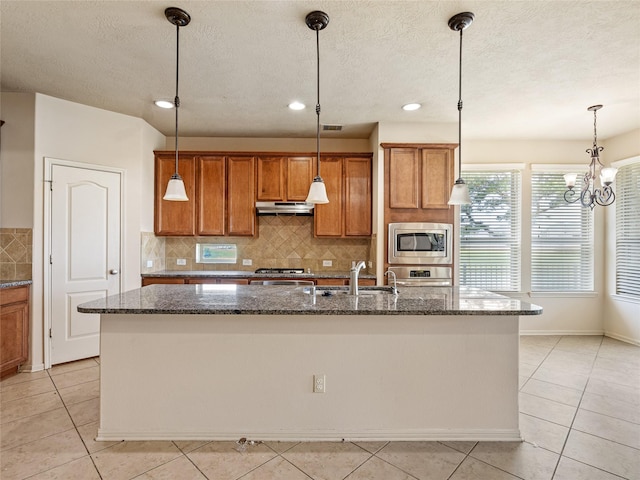 2513 Crestmoon Ct, Houston, TX 77089 - kitchen with brown cabinets, under cabinet range hood, stainless steel microwave, light tile patterned floors, and an island with sink