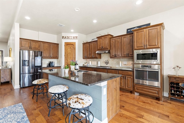 2928 San Milan Pass, Round Rock, TX 78665 - kitchen with stainless steel appliances, a breakfast bar area, light wood-style floors, a center island with sink, and dark stone countertops