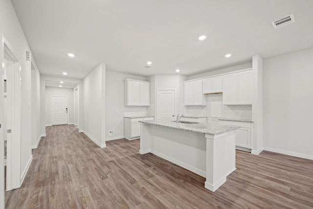 25033 Pomegranate Pl, Montgomery, TX 77316 - kitchen featuring light wood finished floors, recessed lighting, a kitchen island with sink, white cabinets, and light stone countertops