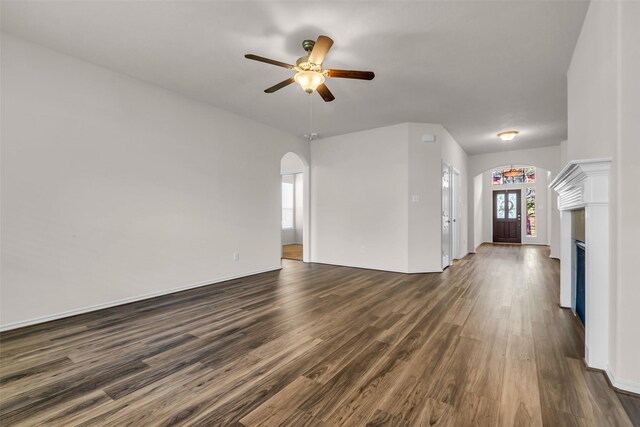 3510 Orchard Valley Ln, Spring, TX 77386 - unfurnished living room with arched walkways, dark wood-style flooring, ceiling fan, and a fireplace