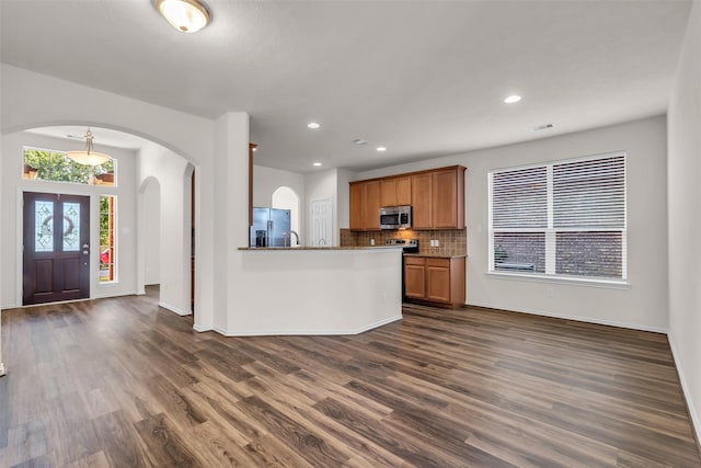 3510 Orchard Valley Ln, Spring, TX 77386 - kitchen featuring appliances with stainless steel finishes, dark wood-style floors, brown cabinetry, arched walkways, and decorative backsplash