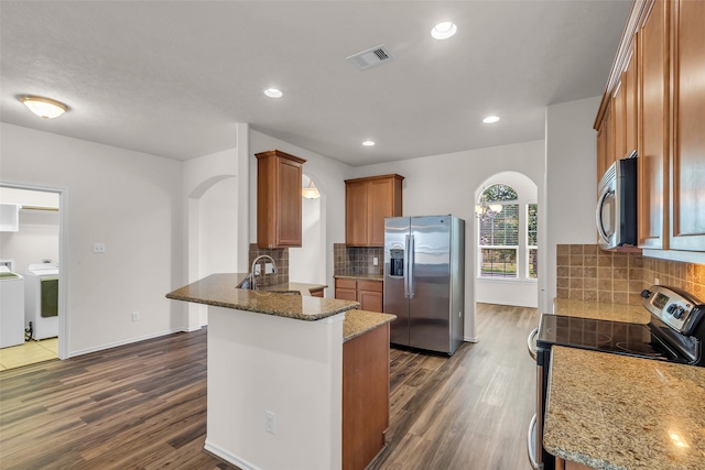 3510 Orchard Valley Ln, Spring, TX 77386 - kitchen featuring appliances with stainless steel finishes, independent washer and dryer, a peninsula, brown cabinets, and dark wood-type flooring