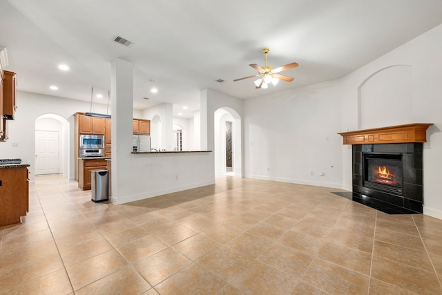 21510 Briar Landing Ln, Katy, TX 77450 - unfurnished living room with light tile patterned floors, a tiled fireplace, a ceiling fan, recessed lighting, and arched walkways