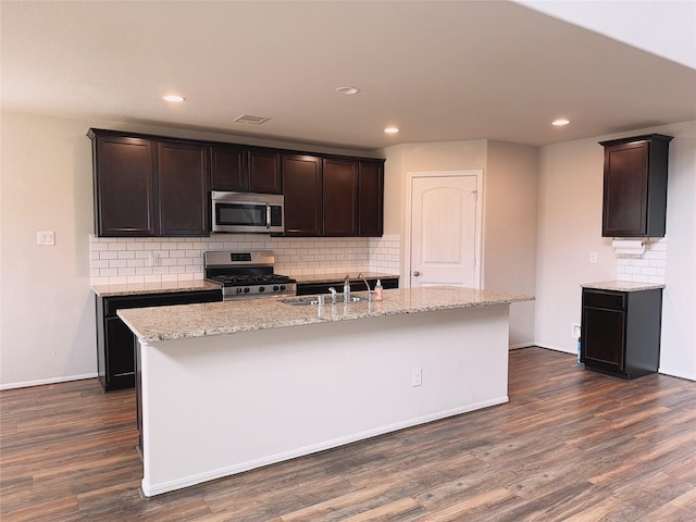 3022 Darlington Ct, Katy, TX 77494 - kitchen featuring appliances with stainless steel finishes, tasteful backsplash, dark wood-type flooring, light stone counters, and a kitchen island with sink