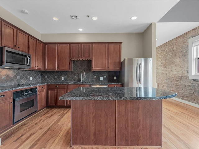 2700 Albany St Unit 3A, Houston, TX 77006 - kitchen featuring stainless steel appliances, light wood finished floors, a center island, brick wall, and dark stone countertops