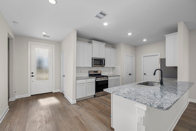 3102 Banyan Dr, Texas City, TX 77510 - kitchen featuring appliances with stainless steel finishes, white cabinets, a peninsula, light wood-style flooring, and light stone counters