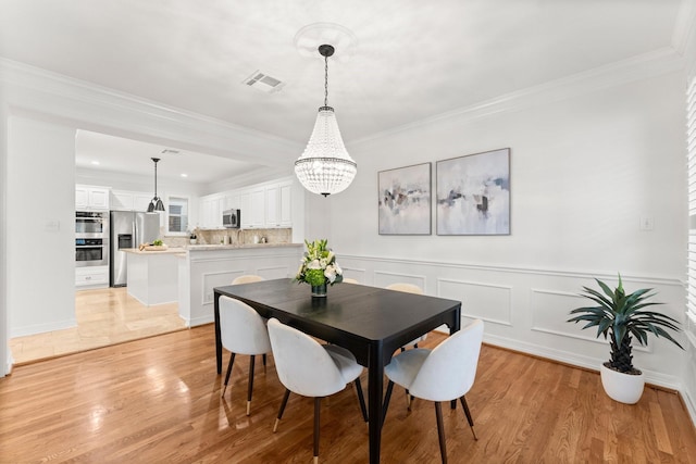 817 Rosine St, Houston, TX 77019 - dining room featuring a chandelier, crown molding, light wood-style floors, and a wainscoted wall