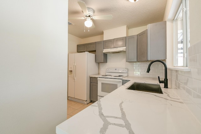 1117 Delores St, Kemah, TX 77565 - kitchen with white appliances, under cabinet range hood, gray cabinetry, decorative backsplash, and light stone counters