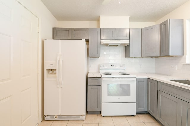 1117 Delores St, Kemah, TX 77565 - kitchen with white appliances, gray cabinetry, under cabinet range hood, tasteful backsplash, and light tile patterned floors