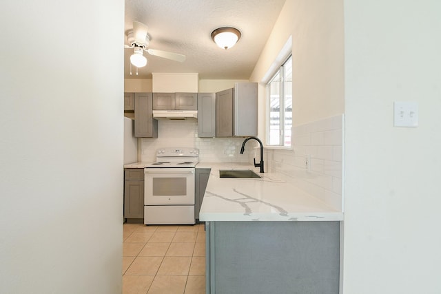 1117 Delores St, Kemah, TX 77565 - kitchen with white electric stove, gray cabinets, under cabinet range hood, decorative backsplash, and light tile patterned floors