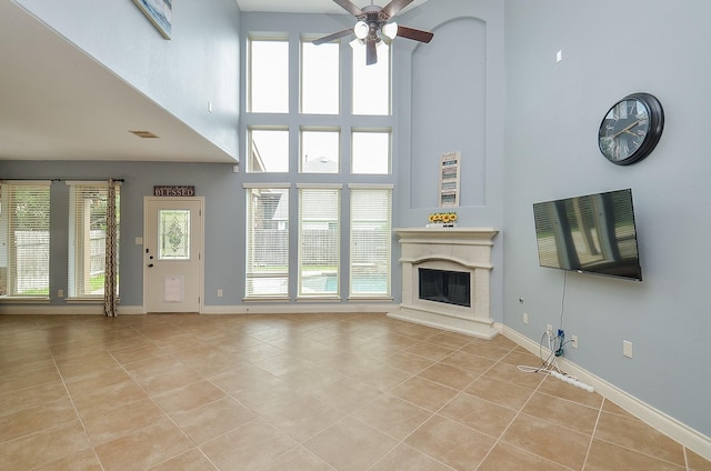 28722 Maple Red Dr, Katy, TX 77494 - unfurnished living room with light tile patterned flooring, a high ceiling, a glass covered fireplace, ceiling fan, and plenty of natural light