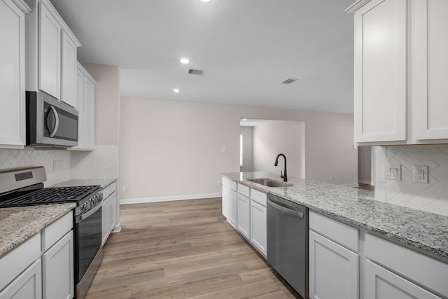 1931 June Lake Ln, Iowa Colony, TX 77583 - kitchen featuring appliances with stainless steel finishes, white cabinets, light wood finished floors, tasteful backsplash, and light stone countertops