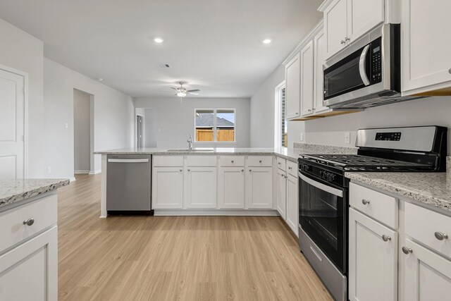 384 Tejas Trl, Waller, TX 77484 - kitchen with stainless steel appliances, a peninsula, a ceiling fan, light wood-style flooring, and white cabinets