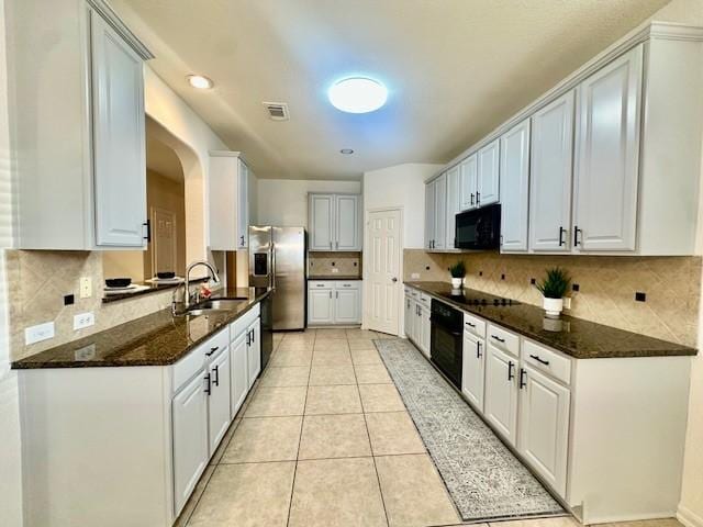 4126 Winesap Bend Dr, Stafford, TX 77477 - kitchen with black appliances, decorative backsplash, dark stone countertops, light tile patterned floors, and arched walkways