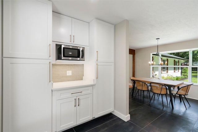 33933 Deer Creek Way, Stagecoach, TX 77355 - kitchen featuring stainless steel microwave, tasteful backsplash, white cabinetry, light countertops, and dark tile patterned flooring