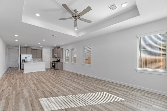 19376 Poppy Village Cir, Magnolia, TX 77355 - unfurnished living room featuring a raised ceiling, healthy amount of natural light, light wood-style floors, and recessed lighting