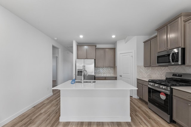 19376 Poppy Village Cir, Magnolia, TX 77355 - kitchen with stainless steel appliances, an island with sink, backsplash, light wood-type flooring, and recessed lighting