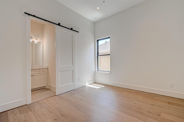 1506 W 43rd St, Houston, TX 77018 - unfurnished bedroom featuring a barn door, light wood finished floors, and connected bathroom